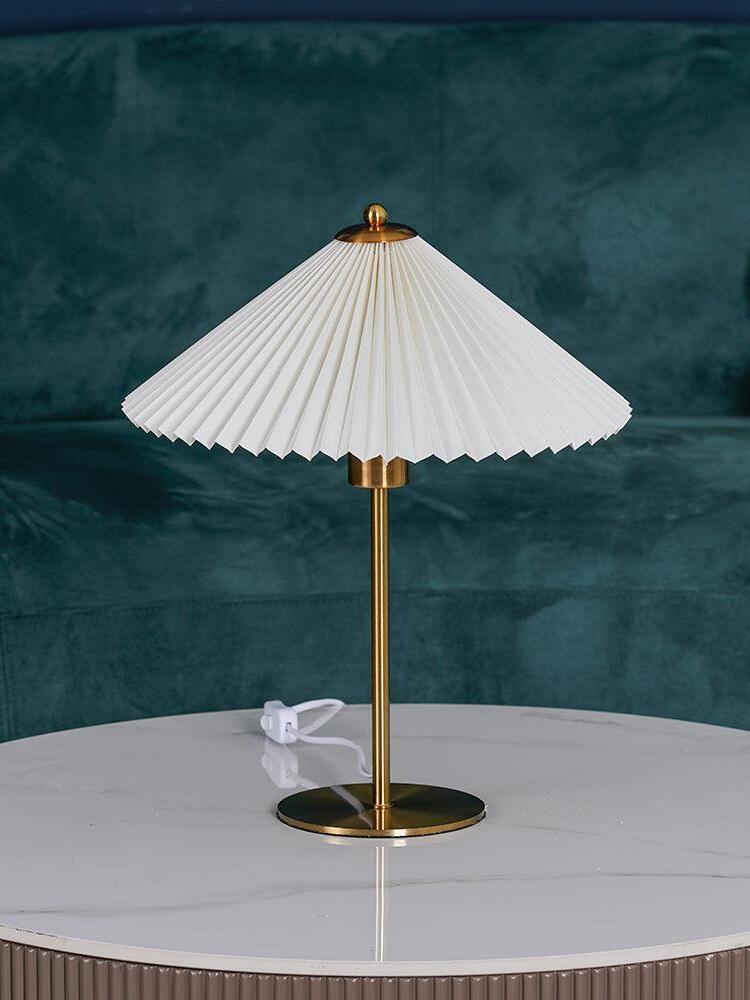 Angled view of the broad pleated shade above the round gold-tone base on a white table