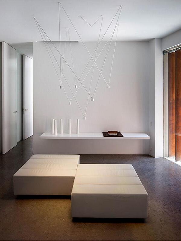 White geometric suspended lights above a wall shelf and white upholstered benches in a modern room