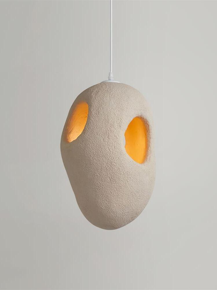 Rounder cream-looking textured pendant with two smaller openings glowing warm inside on a White cord against Gray
