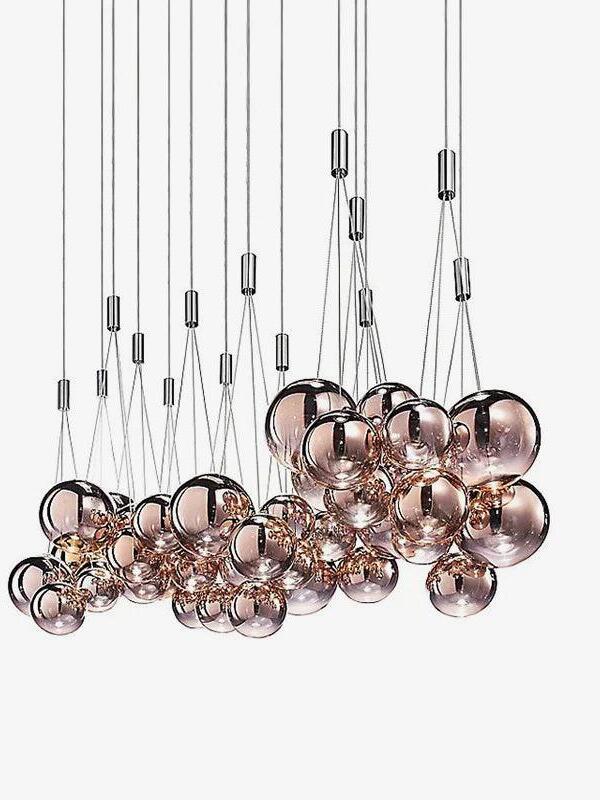 Multiple rose-gold three-globe clusters hanging at staggered heights on white, with thin cords and chrome junction cylinders