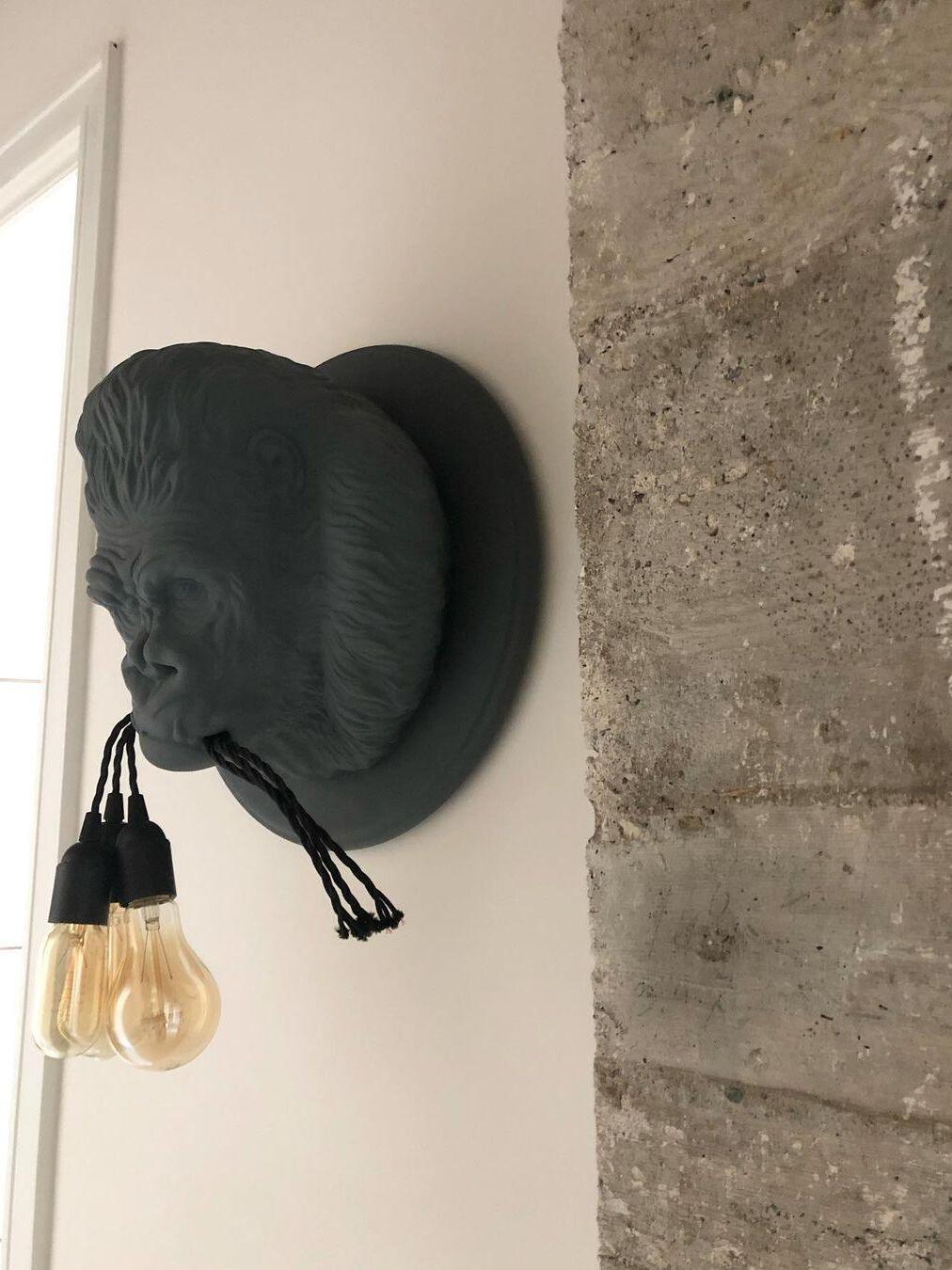 Side view of dark gorilla head and hanging bulbs beside rough wall edge