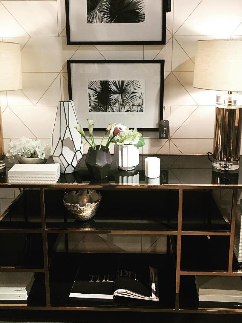 Reflective cylindrical lamp on shelving console beneath framed wall art