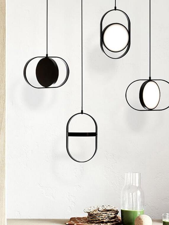 Four black oval-frame pendants with discs turned at different angles above a table with a green drink bottle