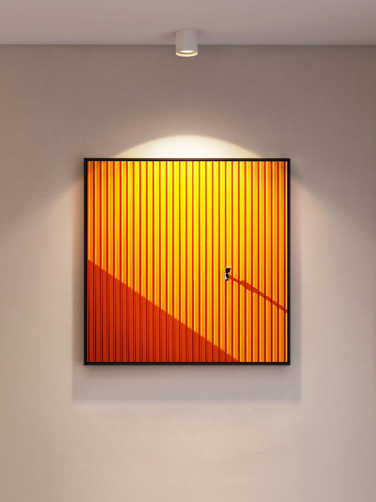 Closer white ceiling light above a large orange architectural print, with a pool of light across the wall