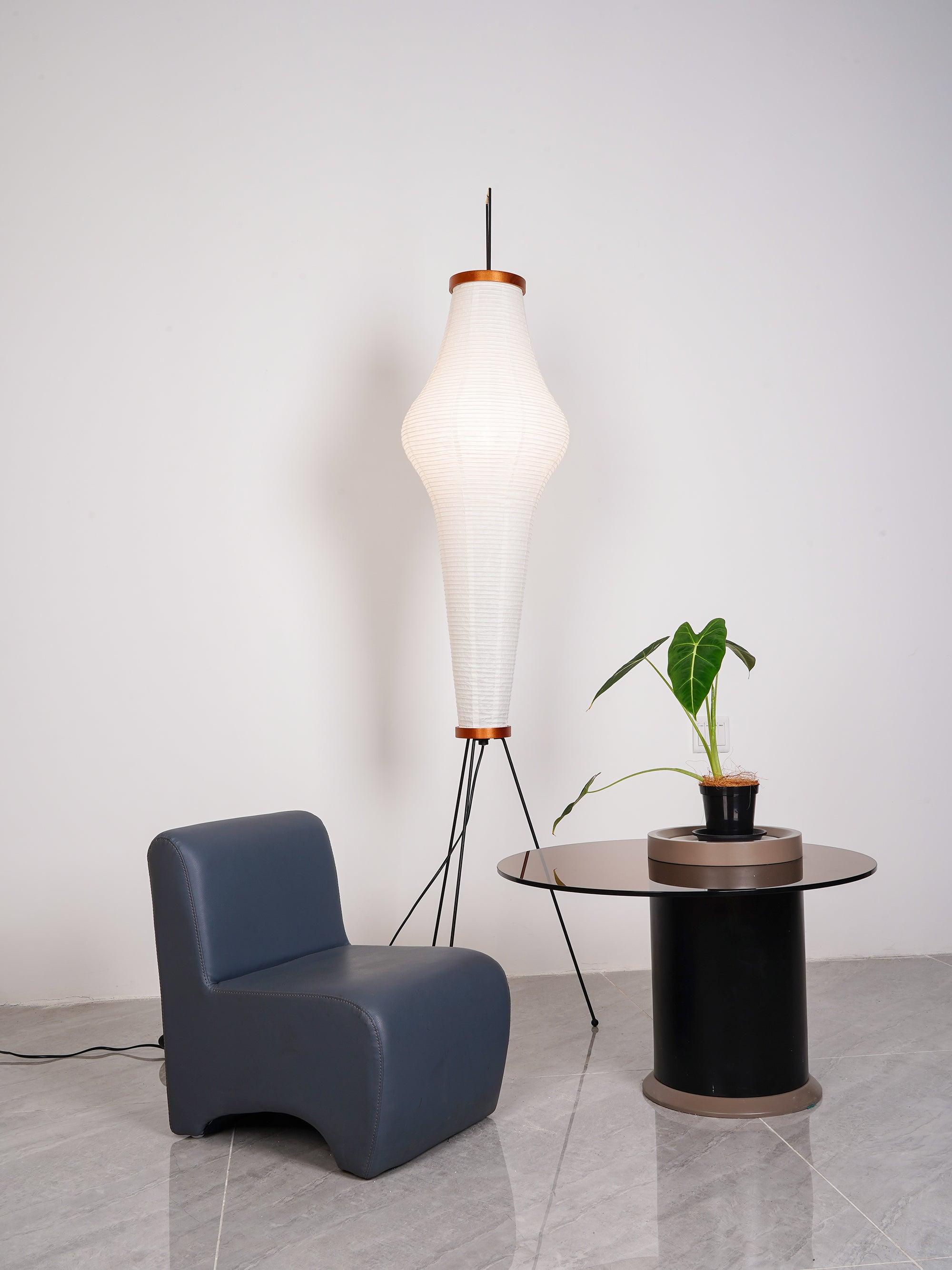 Tall tapered paper lamp with broad upper waist near chair