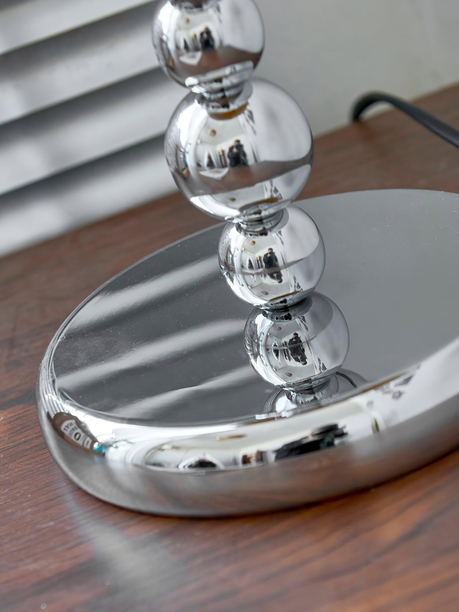 Close-up of the circular chrome base and lower rounded stem on a wooden surface, with a black cord behind