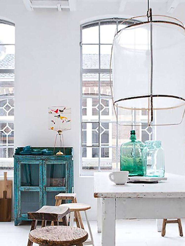 White translucent lantern pendant above white table and green glass bottles, with rustic stools and turquoise cabinet