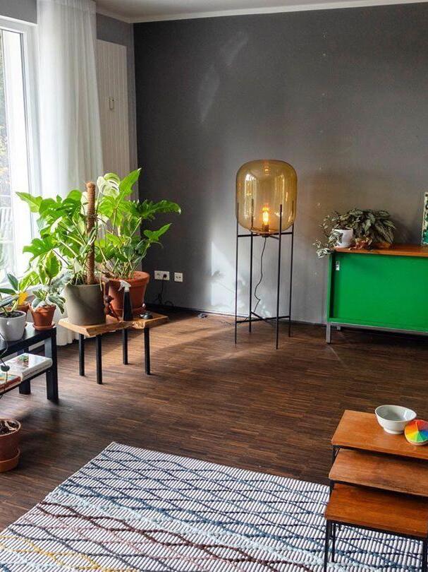 Amber floor lamp on a black stand beside a green cabinet and plants.