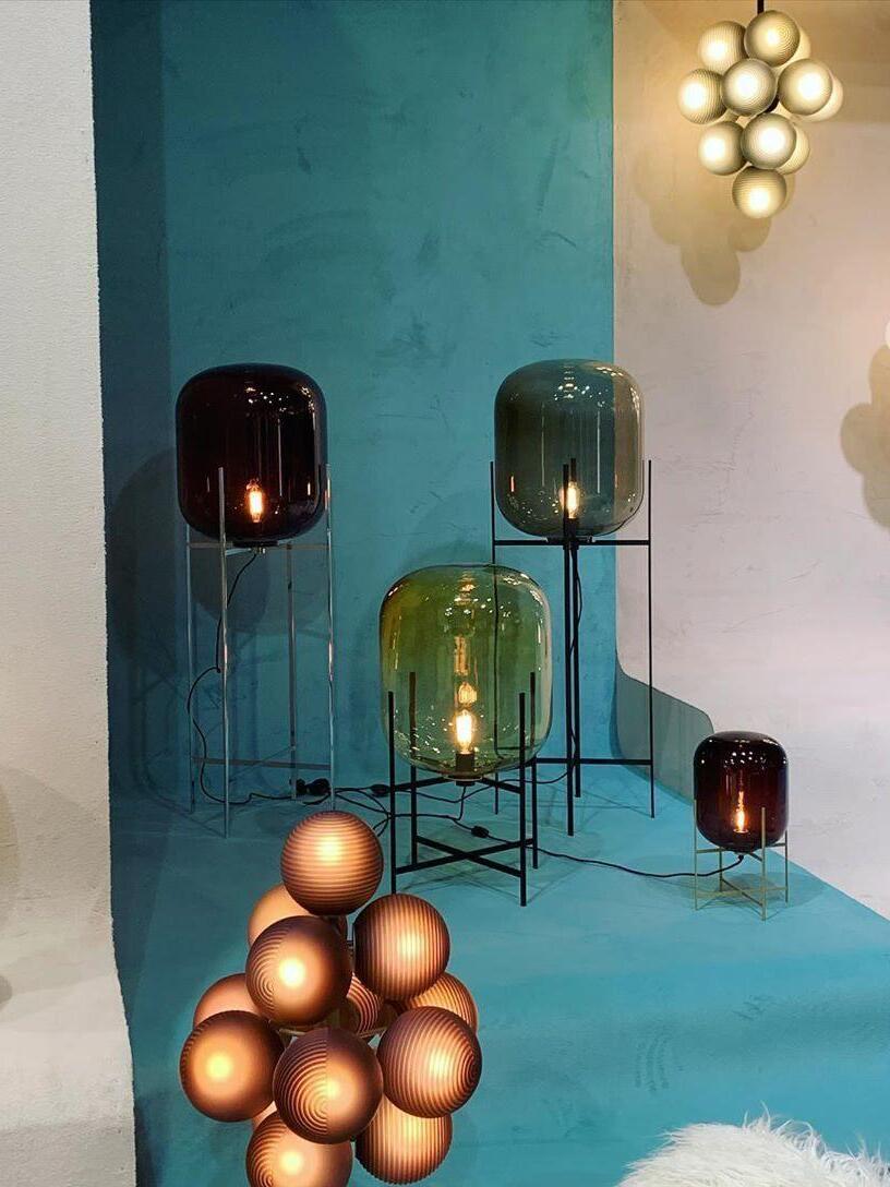 Display of tinted glass lamps on stands of different heights in a blue room.