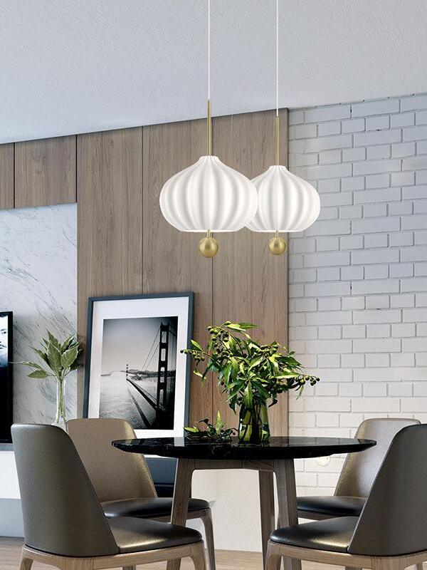 Two white fluted pendants over a round dark table with gray chairs, a plant and a framed bridge photograph