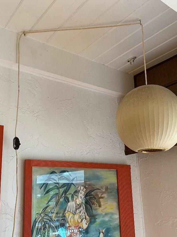 Round ribbed pendant beside framed artwork with a cord routed across ceiling hooks and down the wall