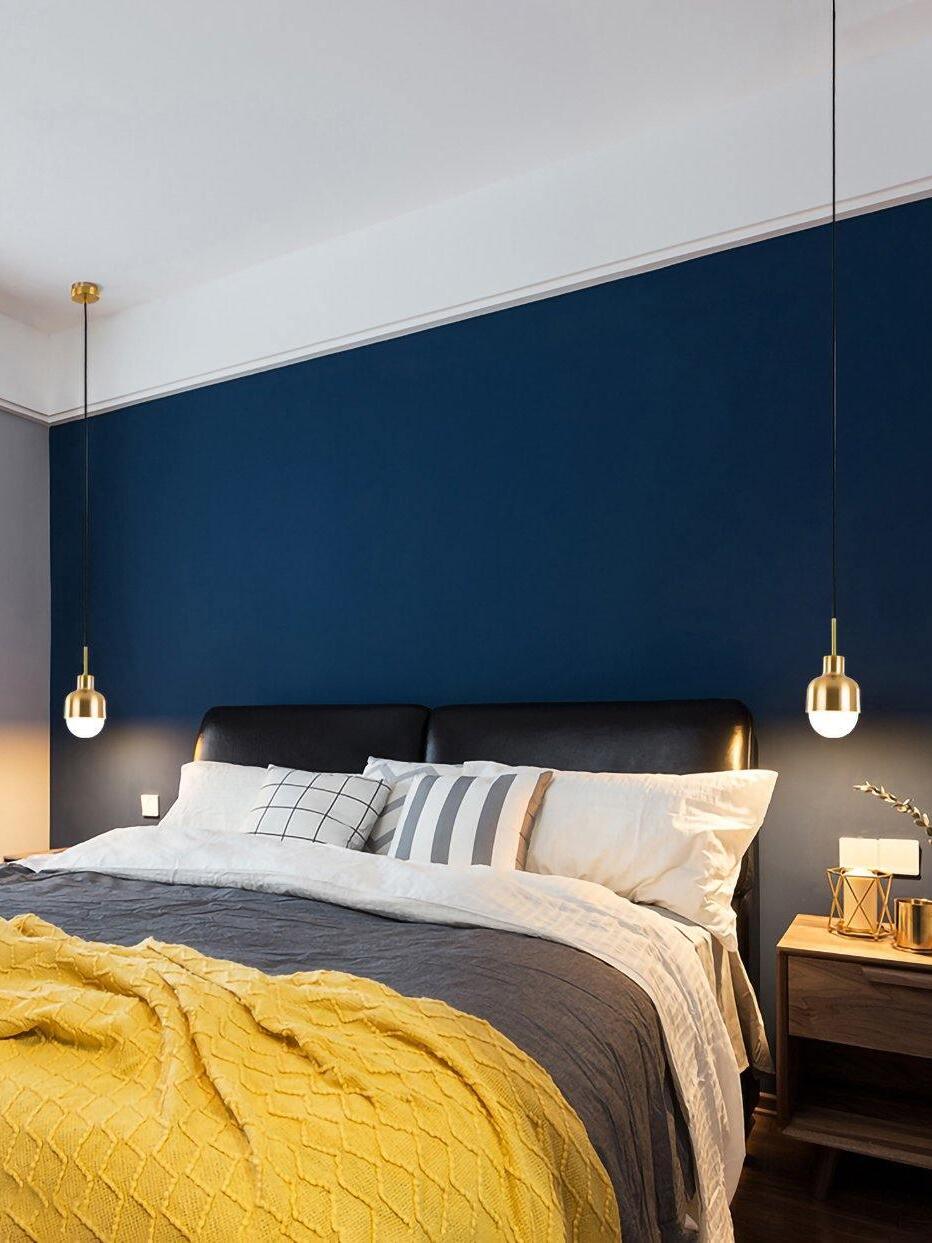 Two lit Niku pendants beside a black headboard against a blue wall, with white pillows and a yellow blanket