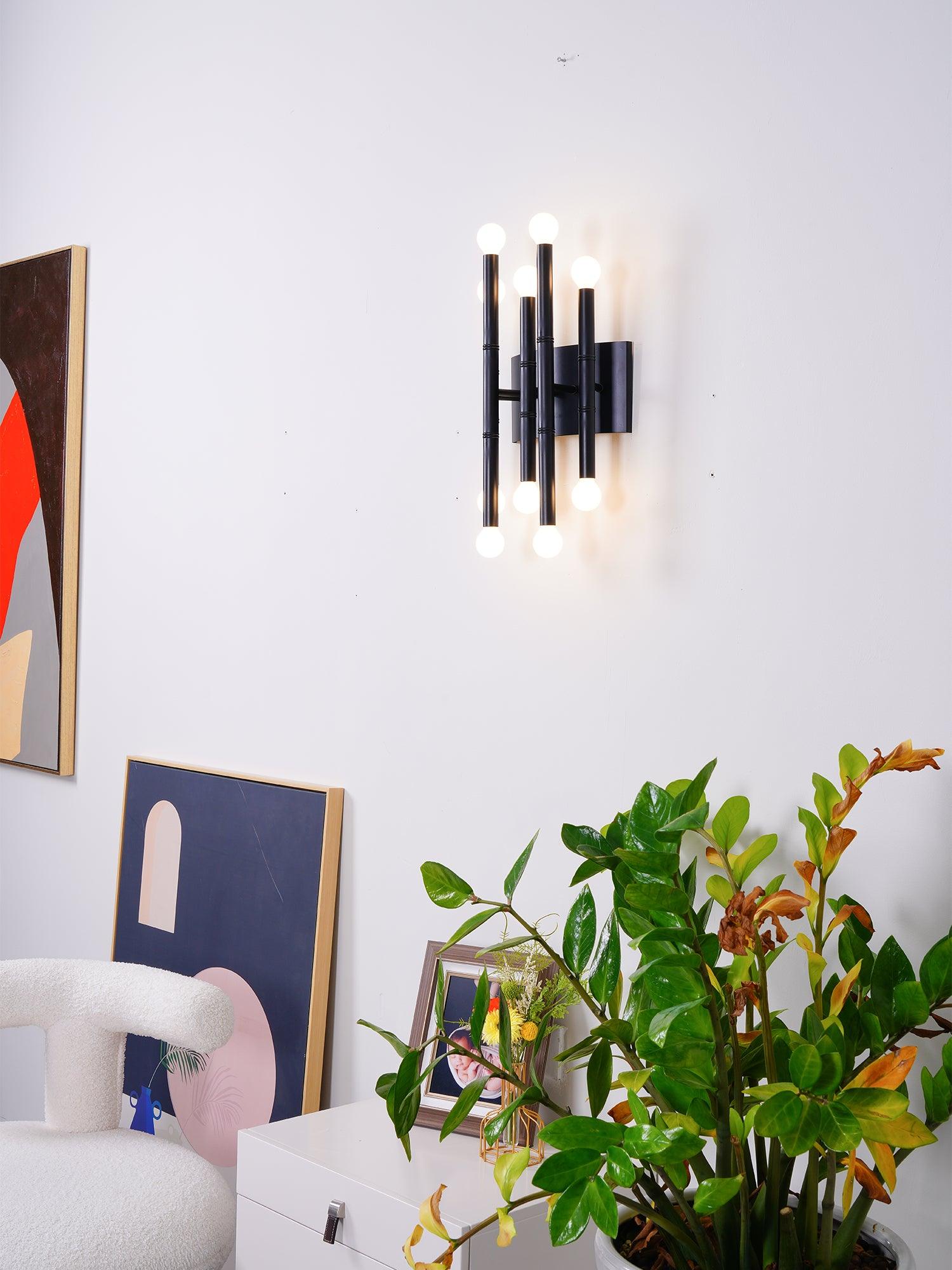 Black Meurice wall light glowing above a console with plants, abstract prints and a textured chair