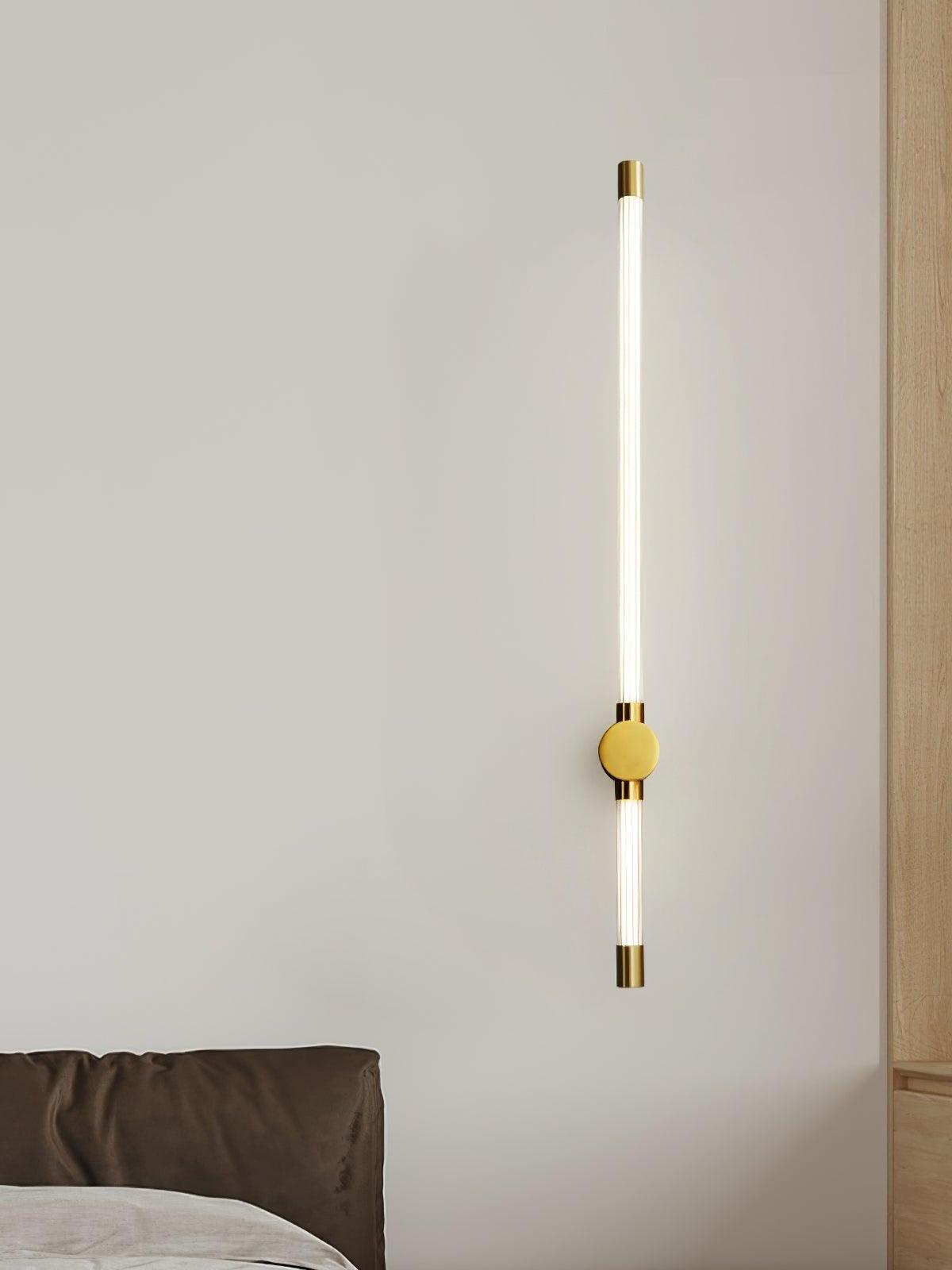 Brass-tone long-and-short tube wall light with a round mount above the edge of a bed