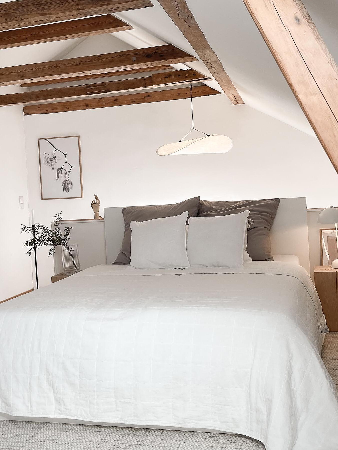 Small white pendant above a bed beneath wood beams