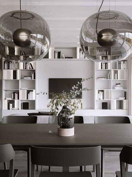 Two dark glass pendants above a dining table in front of bookshelves