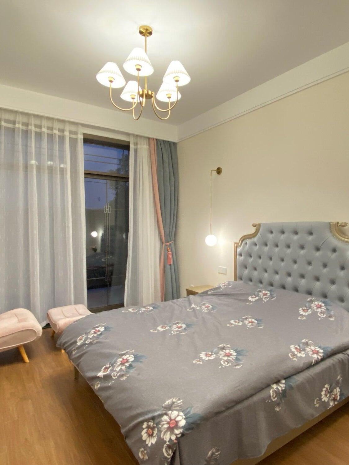 Lenore chandelier above a floral-covered bed beside a tufted headboard and curtains
