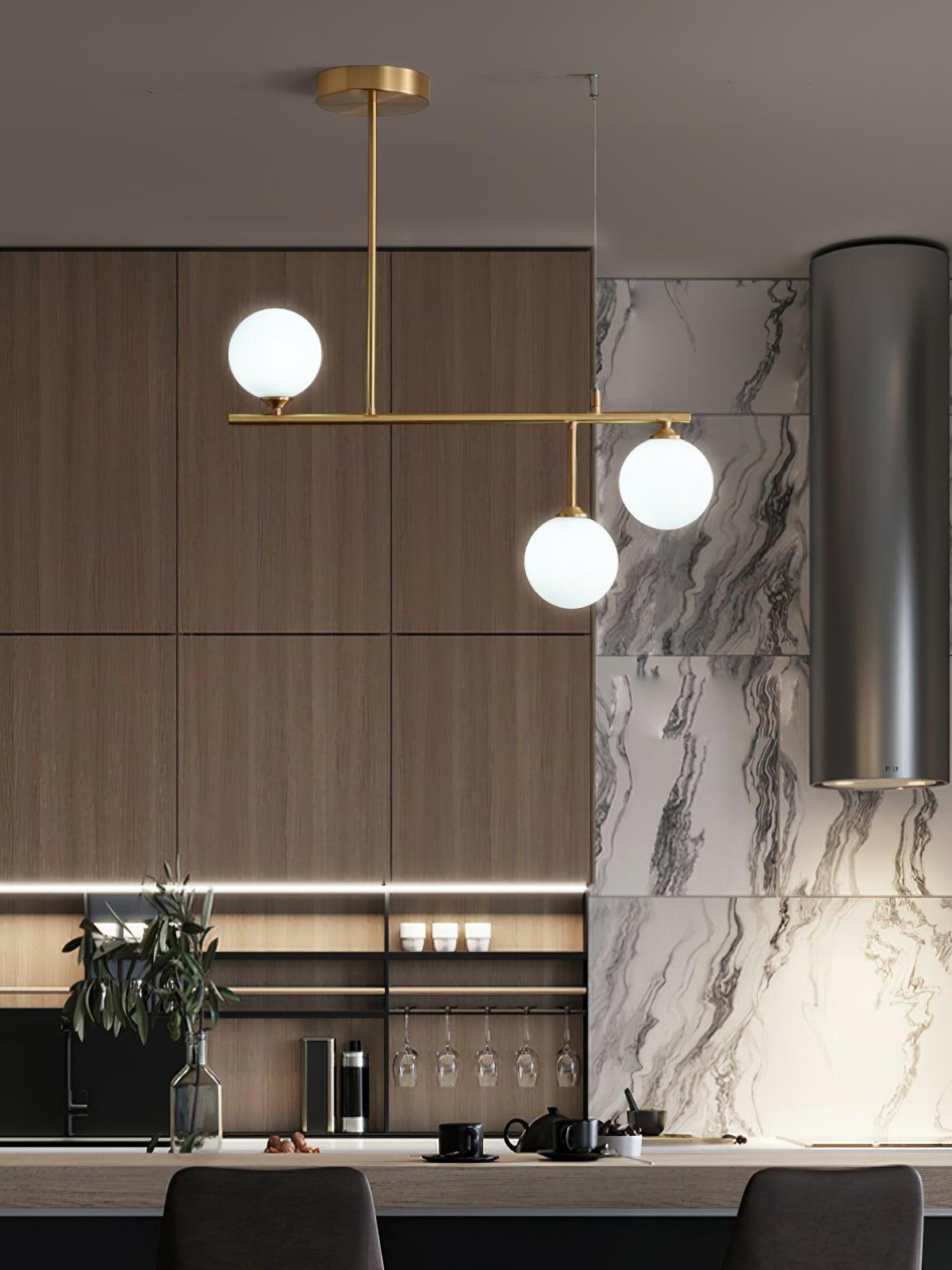 Arteriors three-globe chandelier in a kitchen with wooden cupboards and a veined pale wall