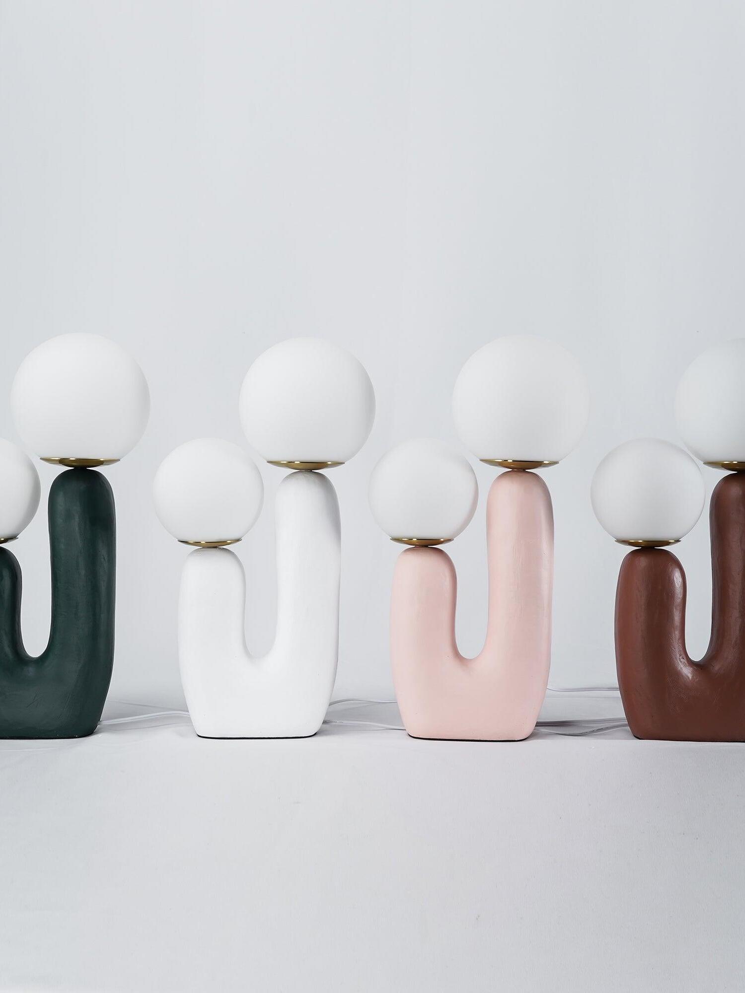 Green, white, pink and terracotta Oo Rough lamps on a pale surface, textured U-shaped bodies and white cords