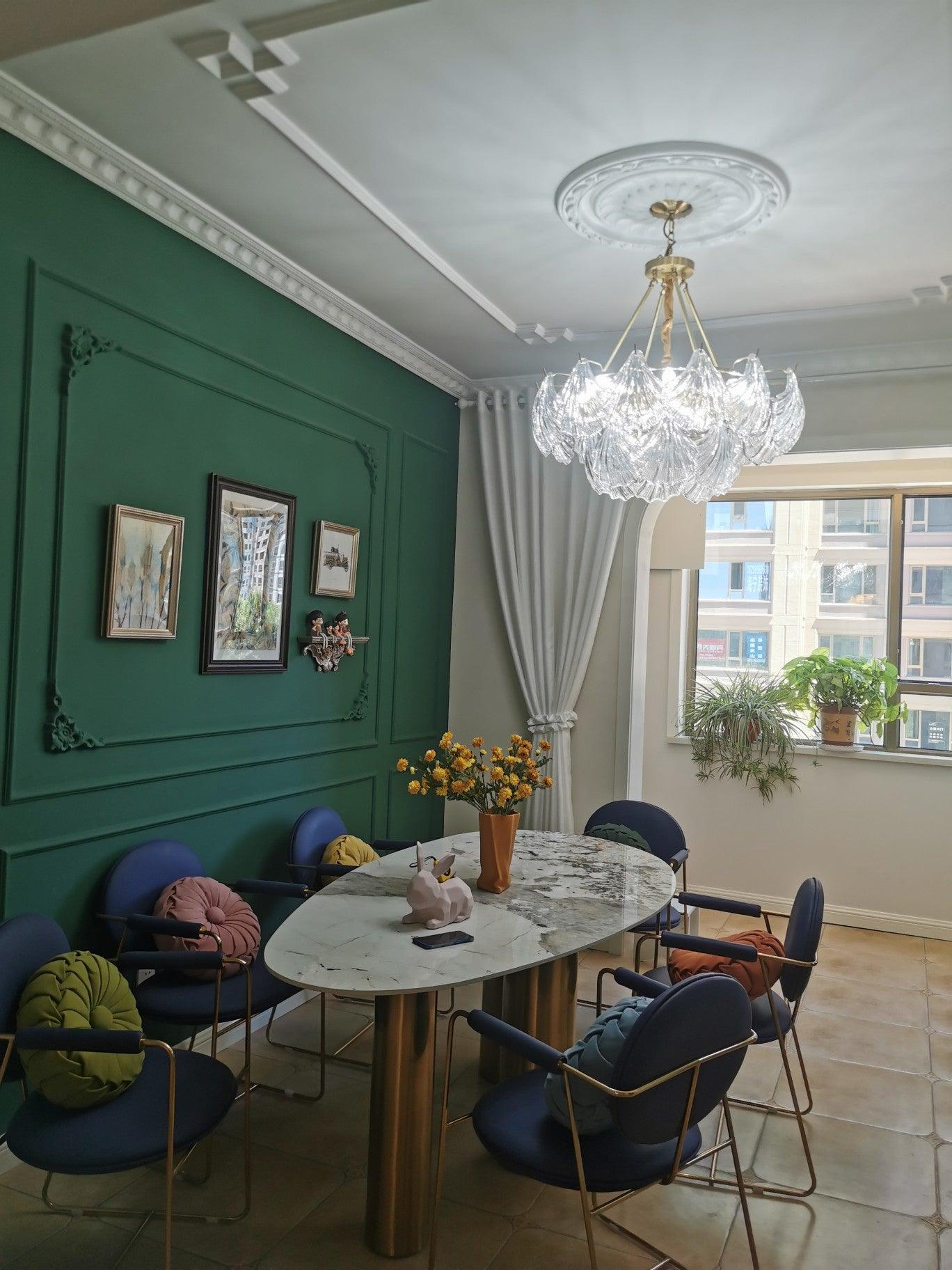 Ribbed glass fixture over a round dining table with blue chairs and a textured green wall