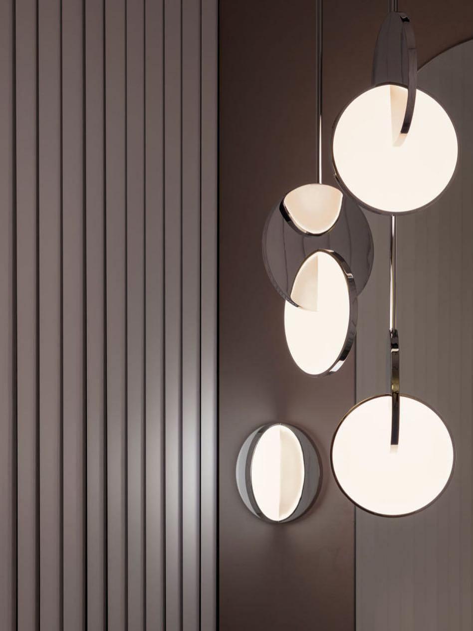 Cropped group of chrome disc pendants and a separate circular wall lamp against dark panels