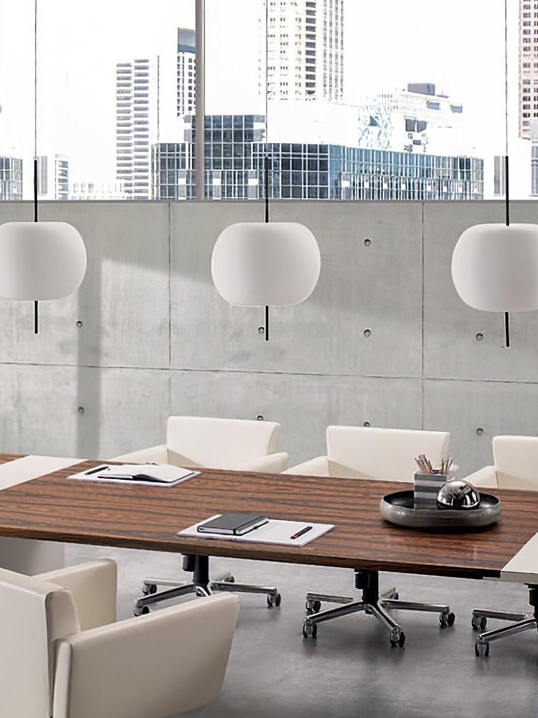 Three white glass pendants above a meeting table beside tall windows