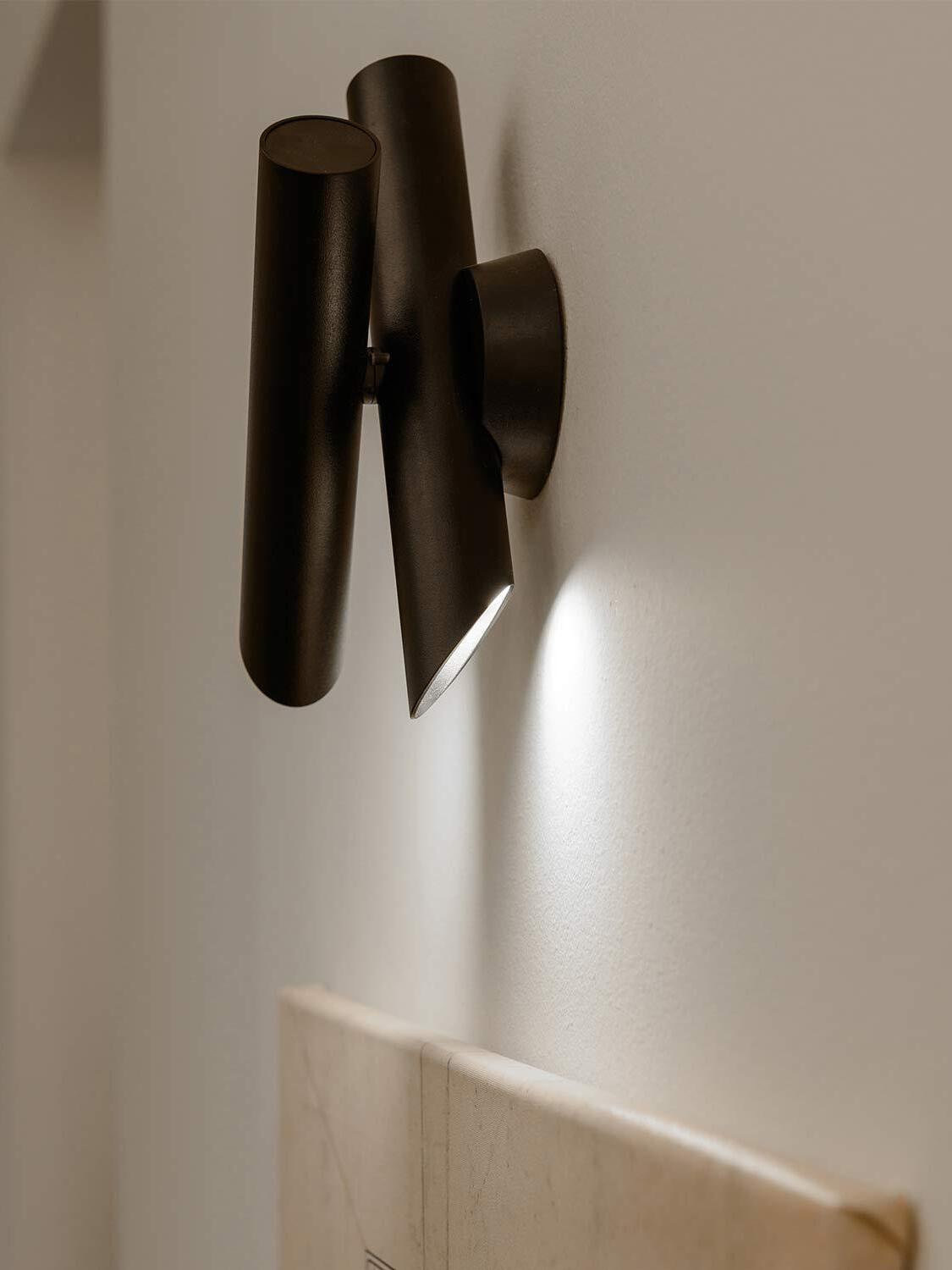 Black crossed tubes casting light down a wall