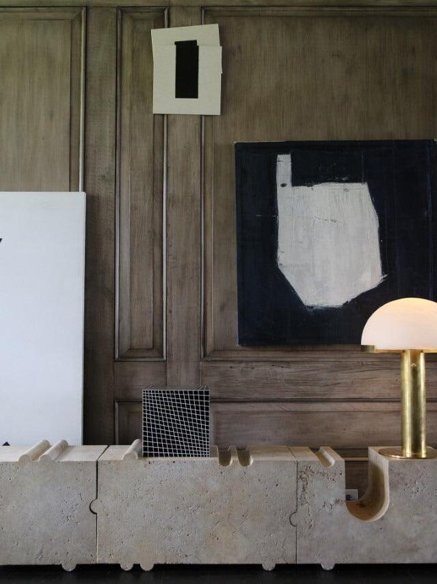 Gold table lamp near artwork and a stone console