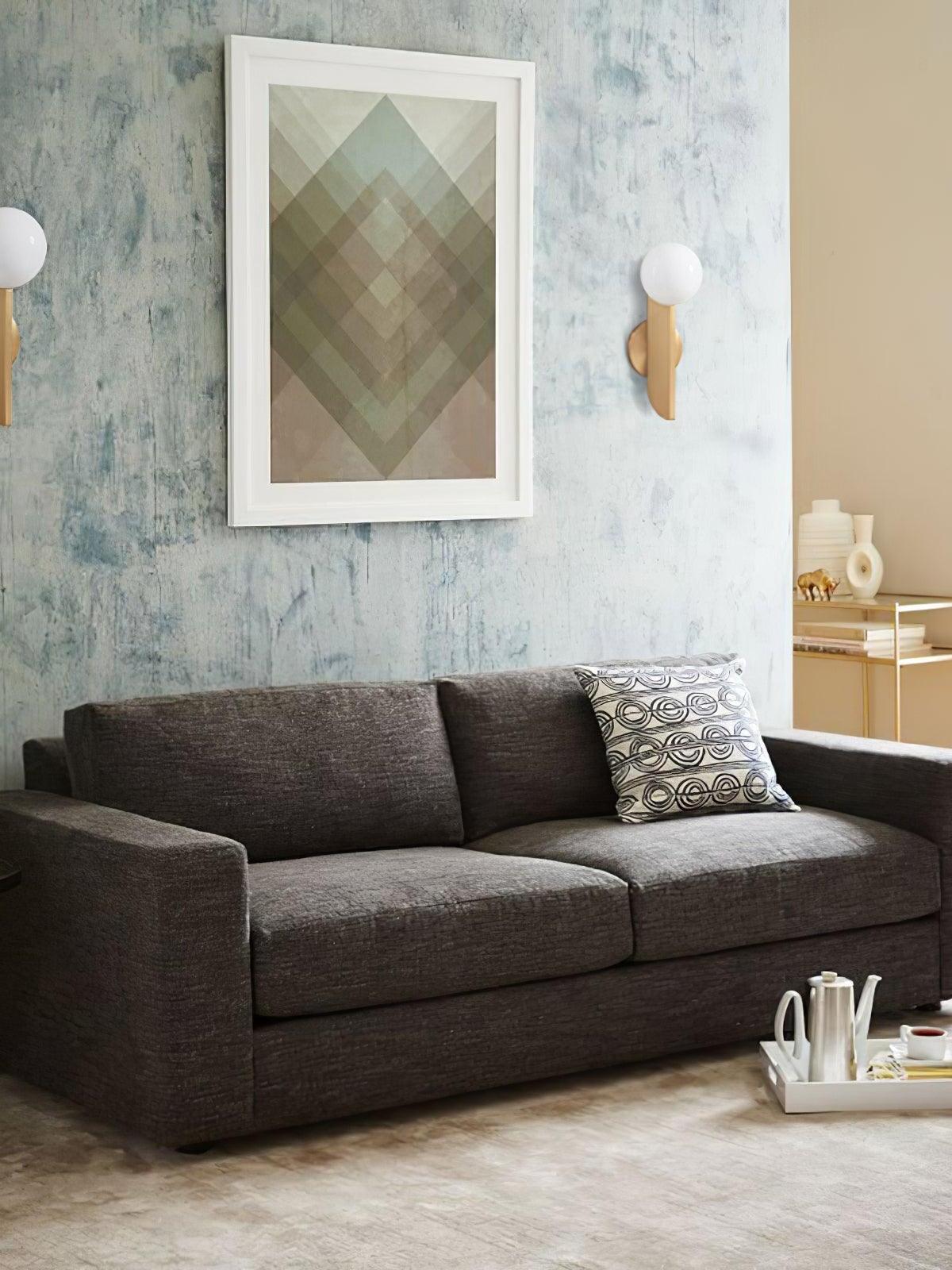Two separate globe wall lights beside framed geometric artwork above a grey sofa, left lamp partly cropped