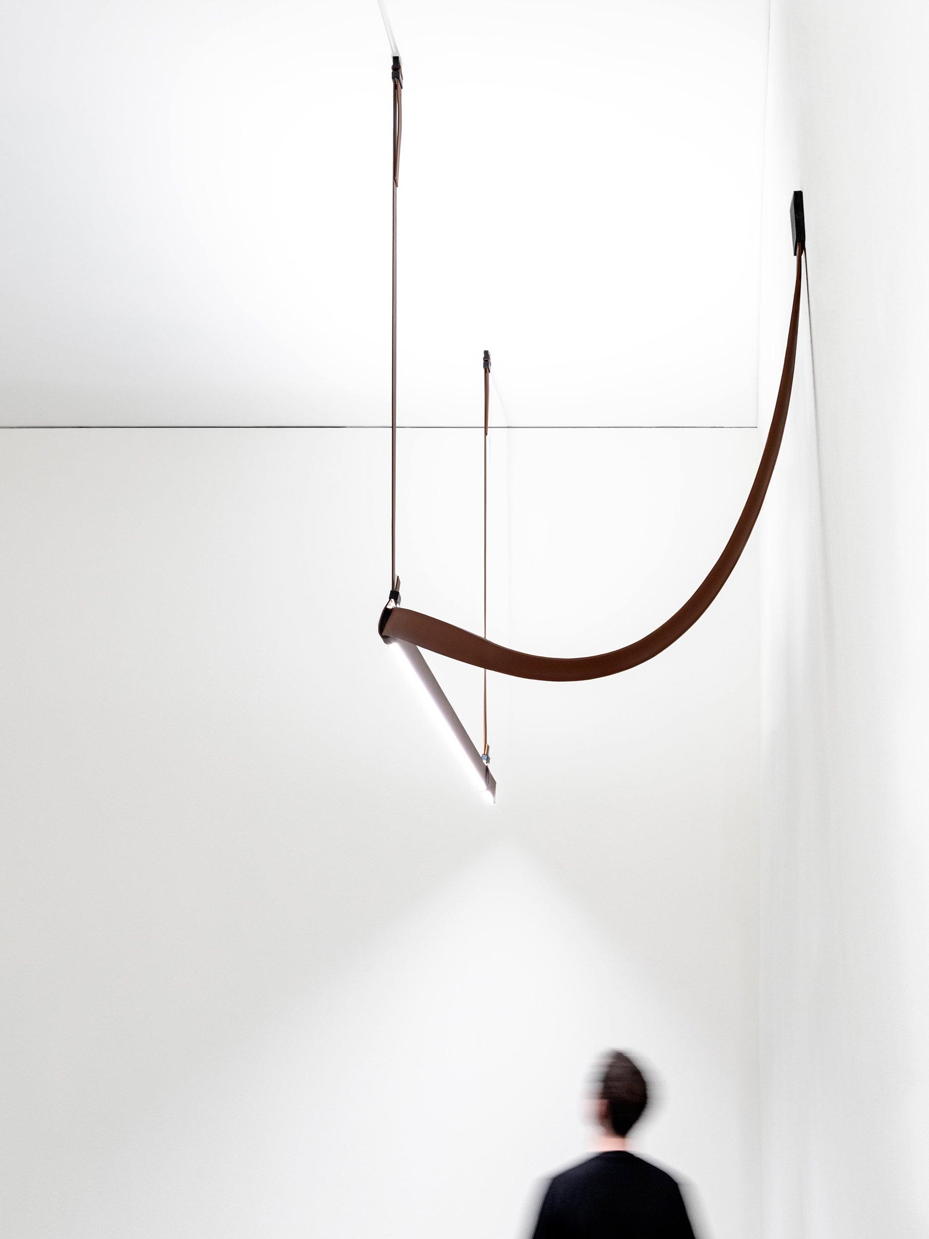 Low-angle view of a brown curved strap meeting an illuminated straight bar, with a blurred person below