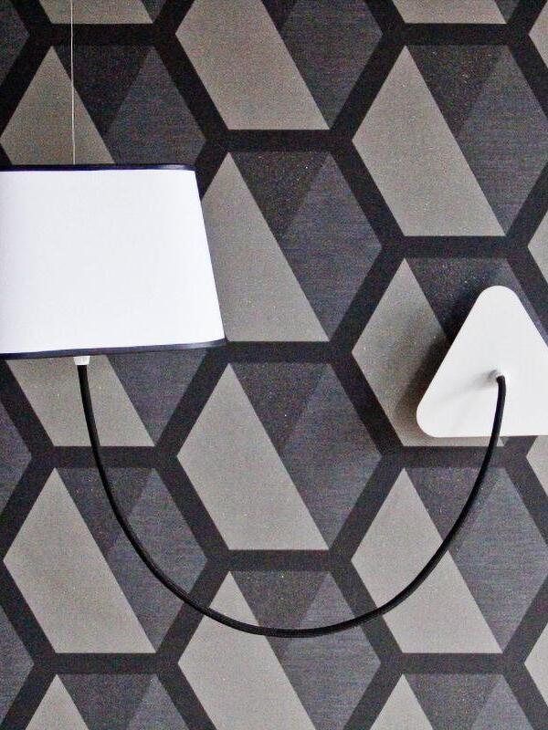 White tapered shade and black cord against patterned wallpaper