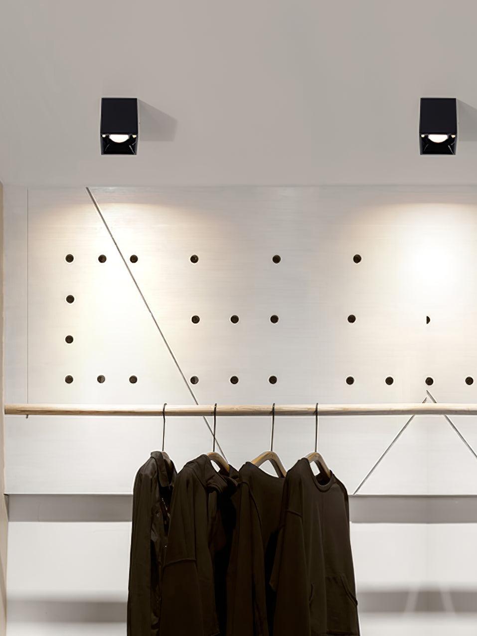 Two black ceiling spots casting light above a clothes rail in front of a pegboard wall