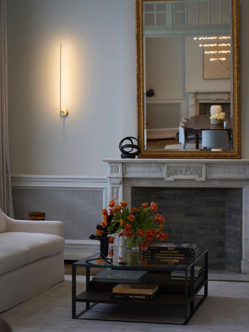 Gold linear wall light beside a mantel mirror