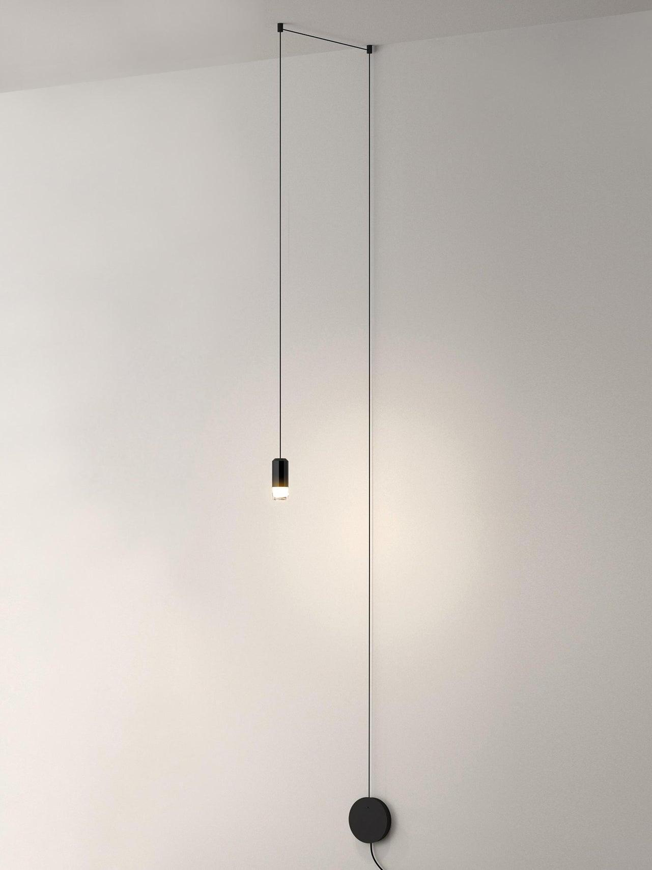 Single lit pendant on ceiling-routed cable beside a round wall plate
