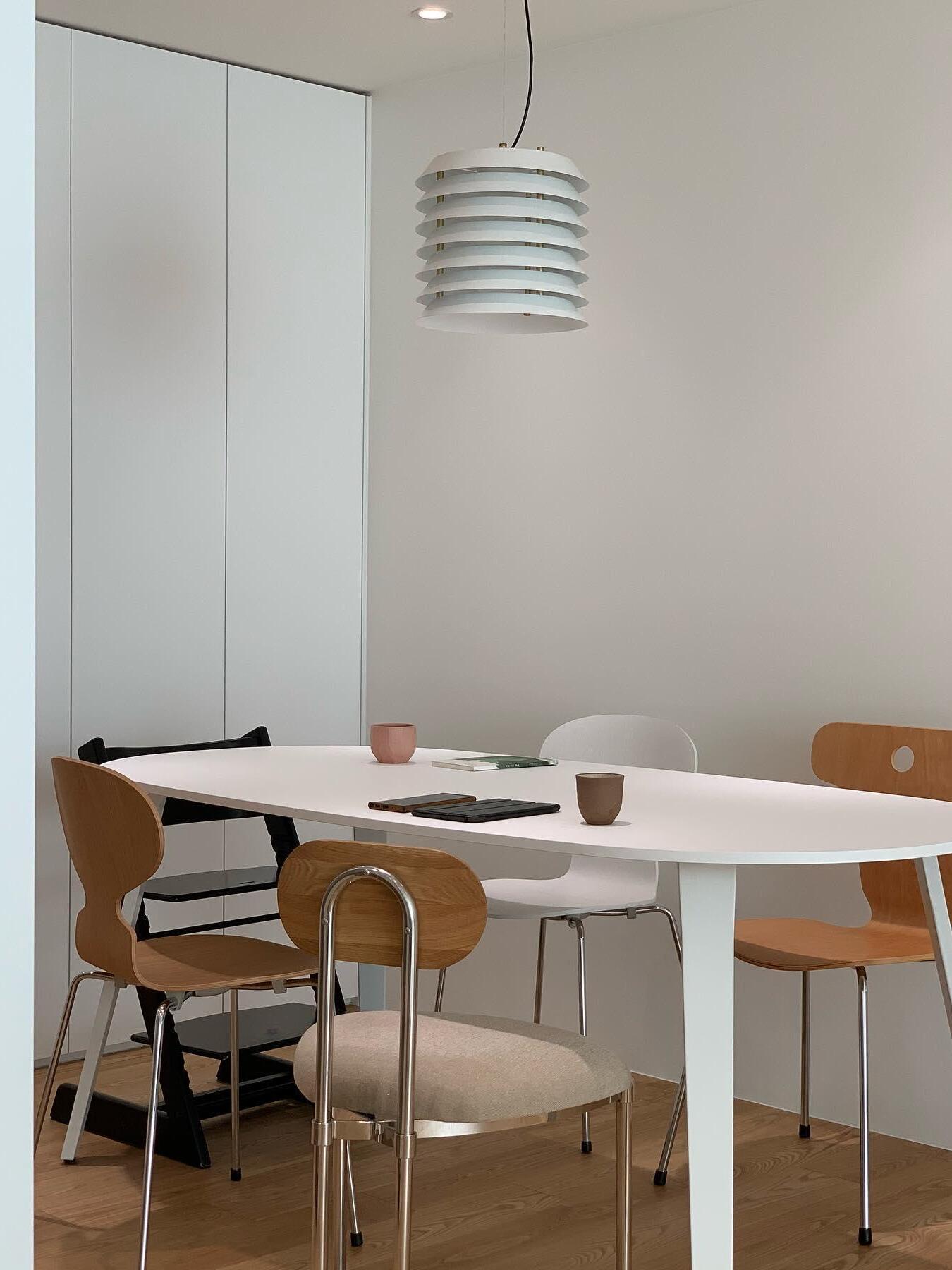 White layered pendant above oval dining table with curved wood chairs
