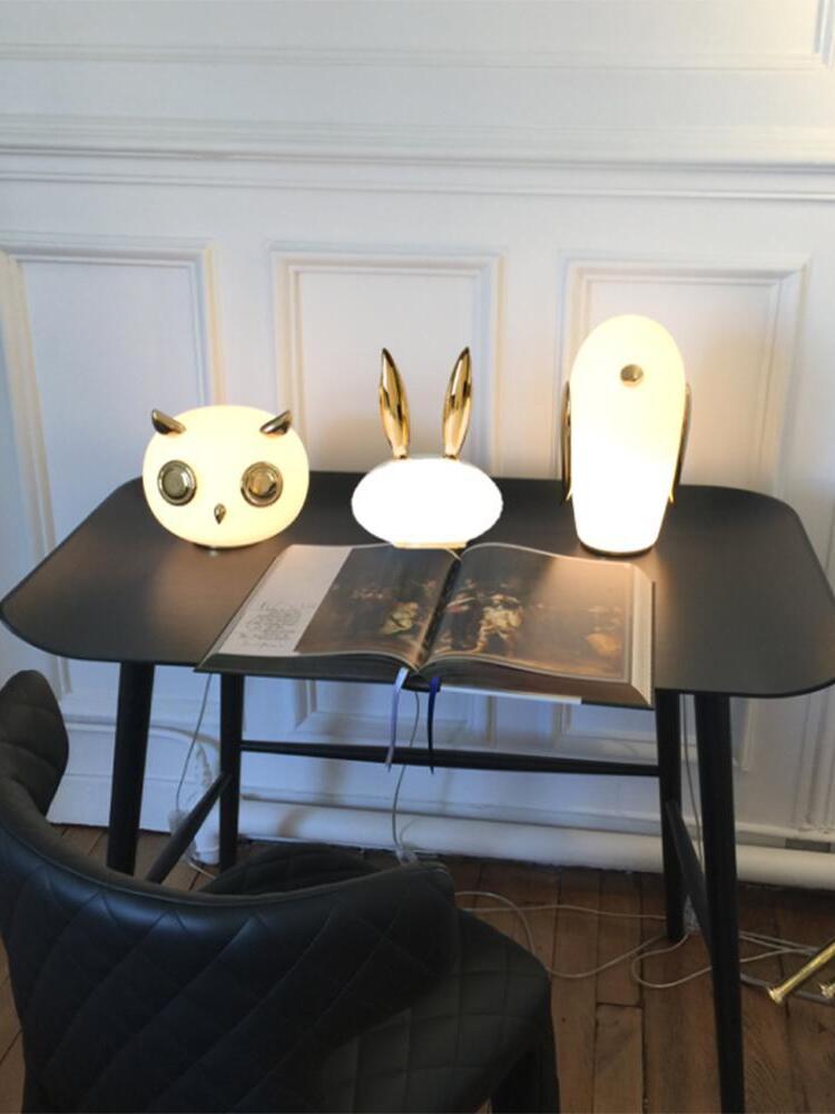 Owl, rabbit and penguin lamps grouped on dark table with open book