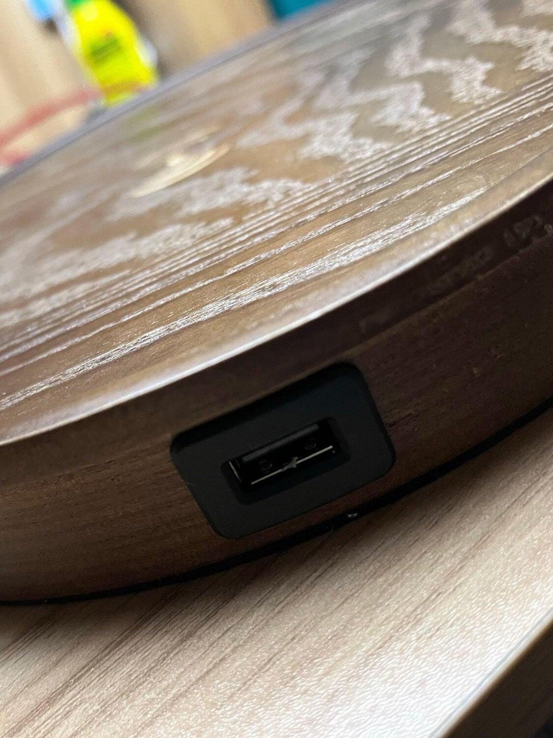 Close-up of the rectangular USB port in the wooden base edge, with worn pale marks on the upper surface