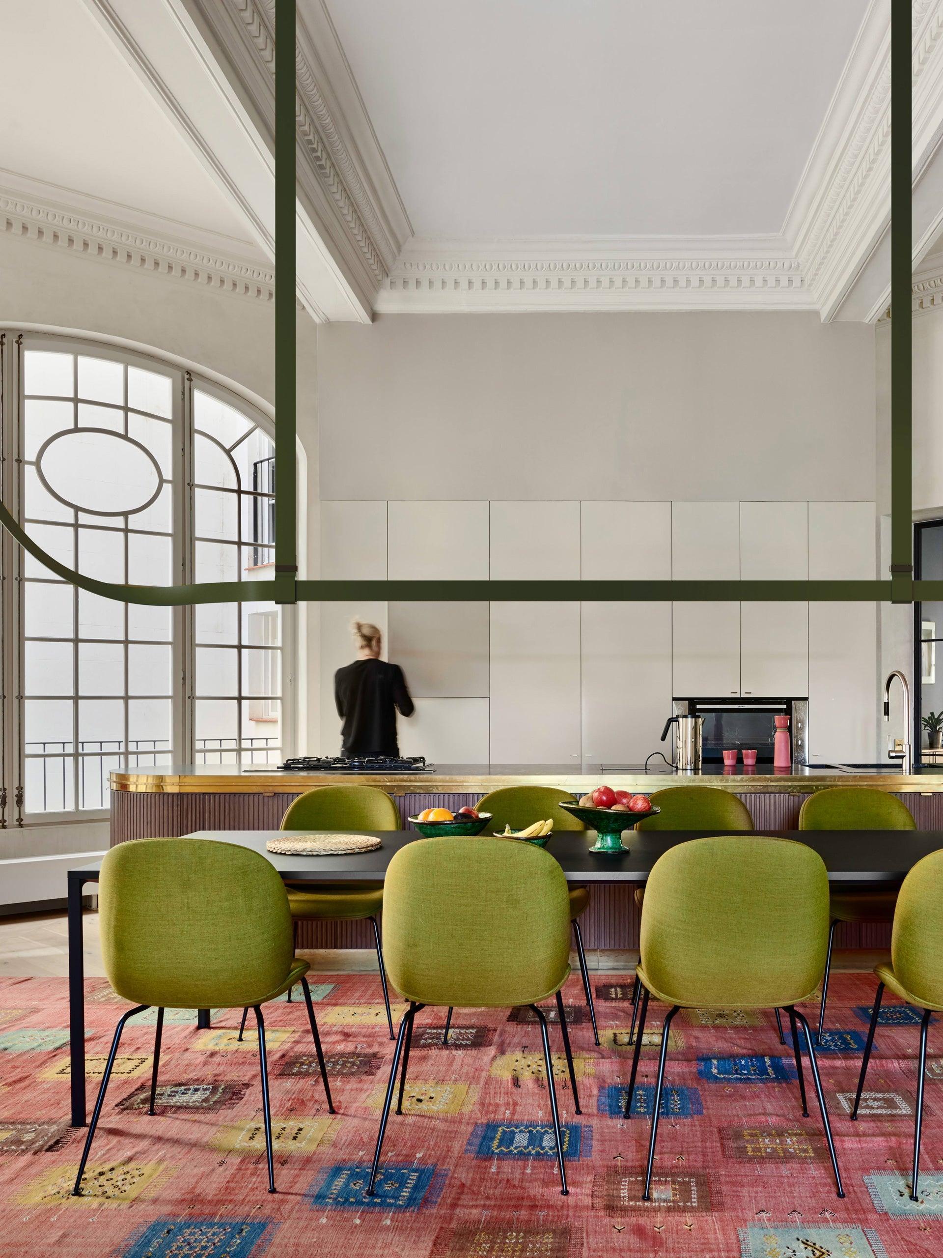 Green belt-shaped pendant above a black table and green chairs in a room with decorative ceiling mouldings