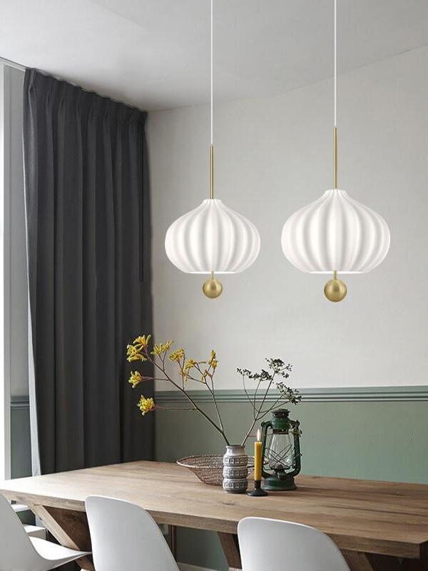 Two white fluted pendants above a wooden table with yellow flowers, a green lantern and white chairs