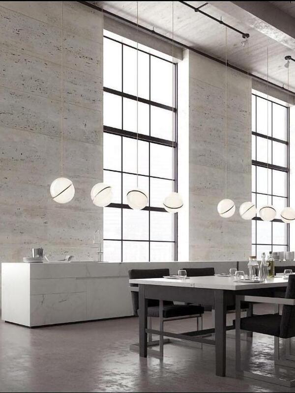 Multiple separately suspended Crescent globe pendants over dining tables in a concrete interior with grid windows