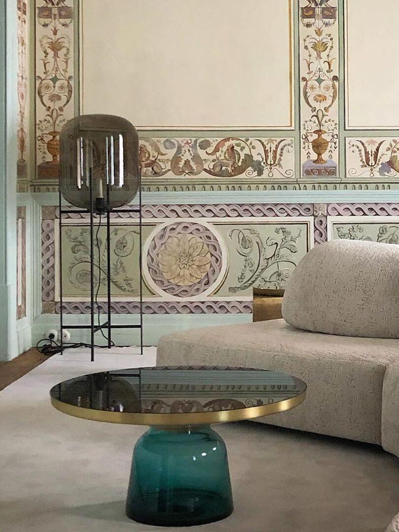Tall grey glass lamp behind a curved sofa in an ornate interior.