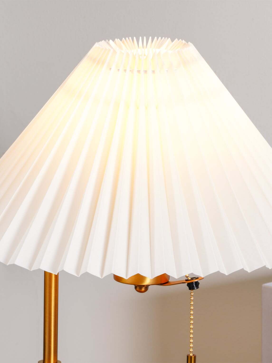Close-up of the illuminated pleated white shade and gold-tone lamp fitting beneath its edge