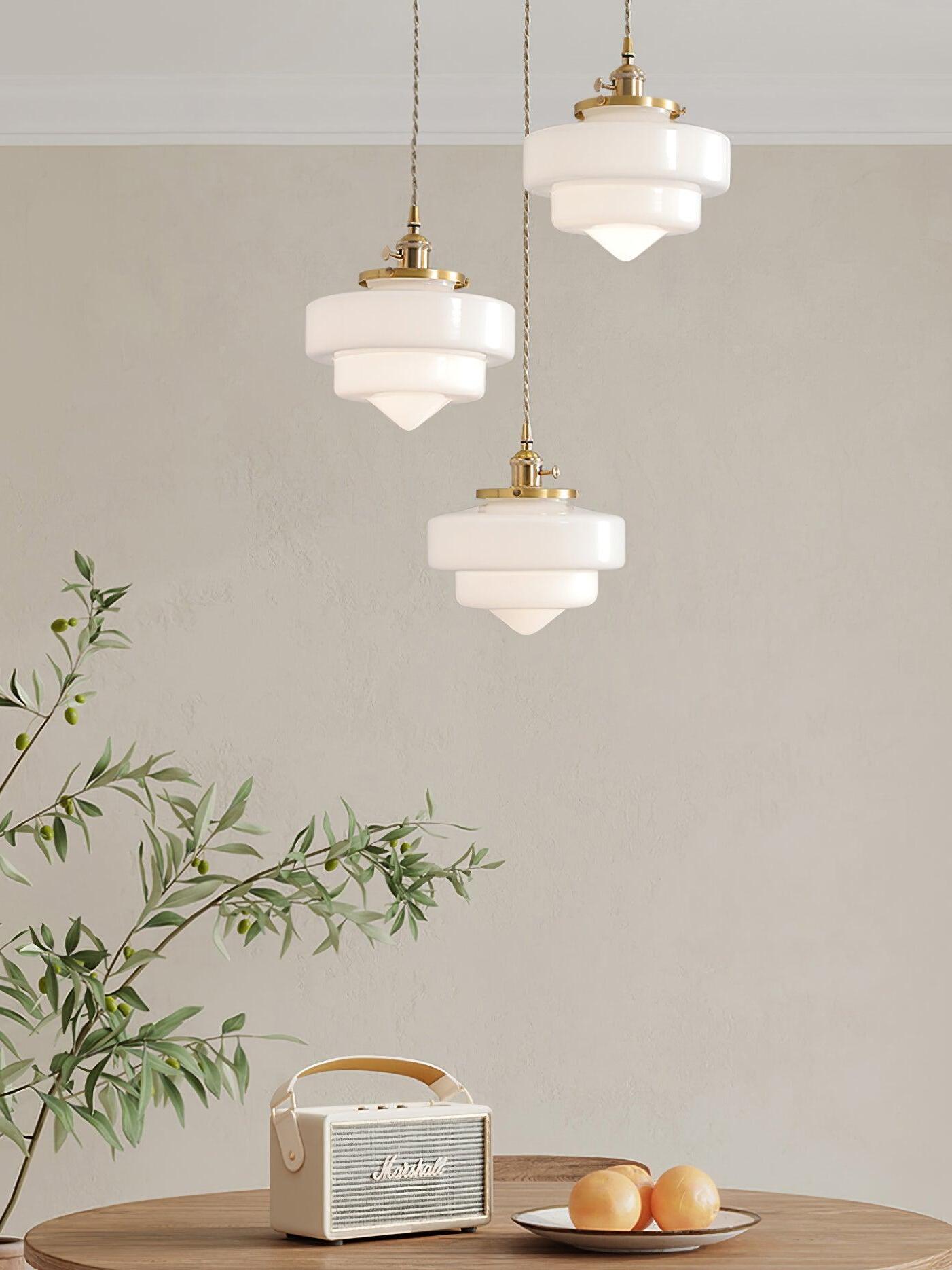 Three staggered lit Atlas Model A shades above a round wooden table with a small radio, fruit and leafy branches