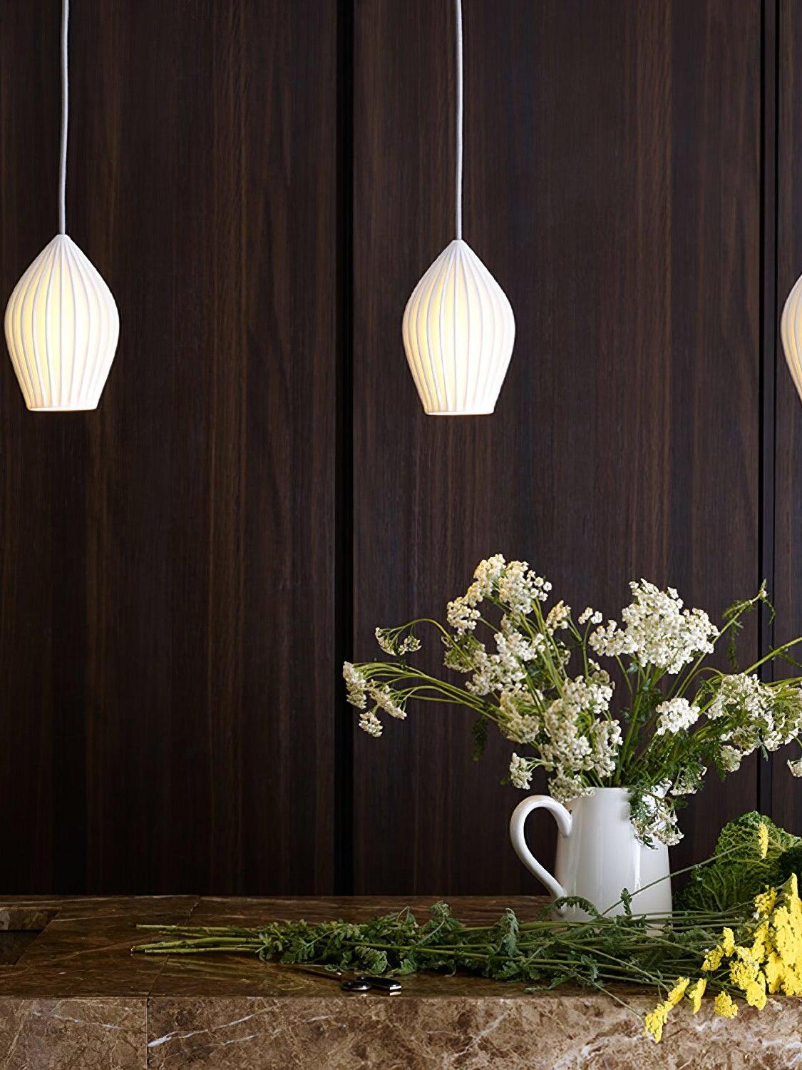 Illuminated ceramic pendants above a table with white flowers against a dark wall