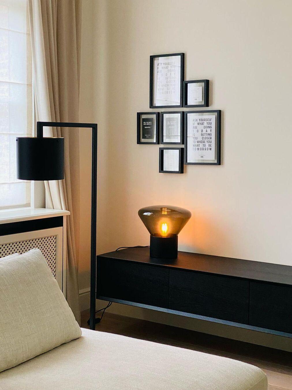 Small amber-lit glass lamp on black console beneath framed wall pictures