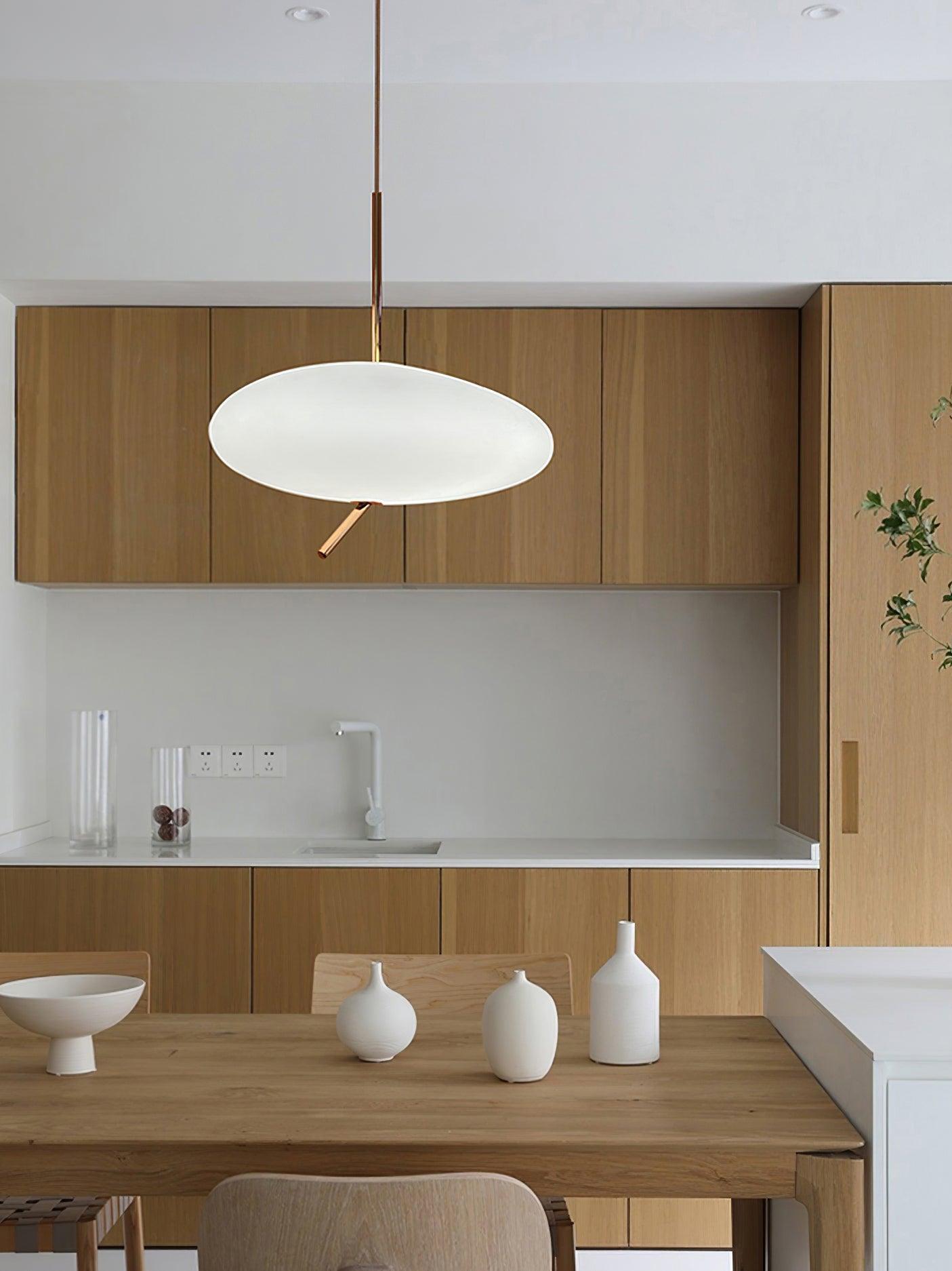 White flattened pendant with a rose-gold stem in front of wood cabinets and a kitchen counter
