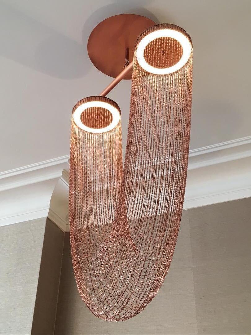 Upward view of rose-gold chain loops, two illuminated rings and a round ceiling canopy