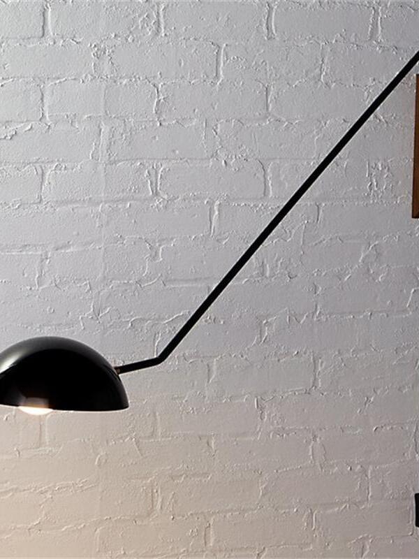 Lit black dome and diagonal arm against a white brick wall, with part of a wooden mounting block at right