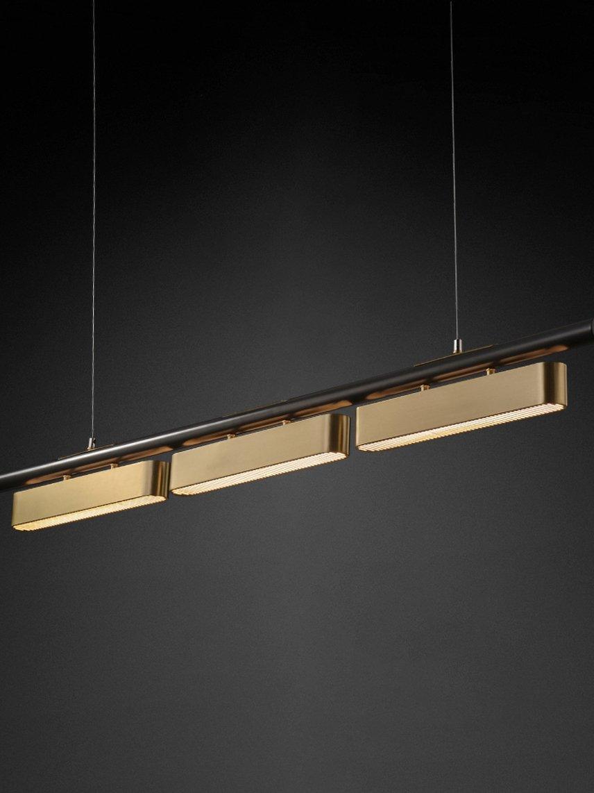 Oblique Colt three-module black-rail pendant against black, with lit brass housings beneath