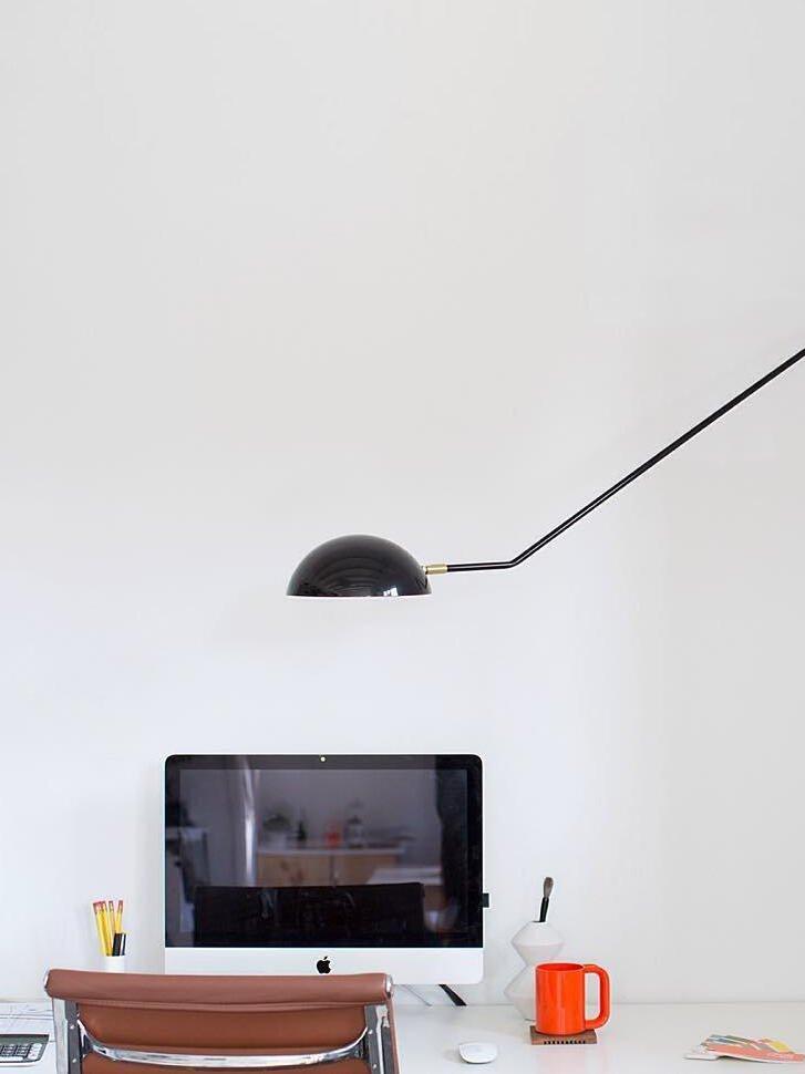 Black dome and angular arm above a desktop computer on a white desk, with brown chair and orange mug